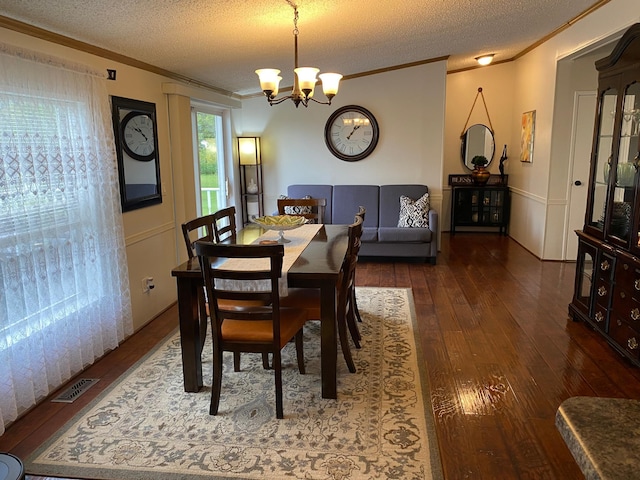 dining space with ornamental molding, a textured ceiling, a chandelier, and dark wood-type flooring