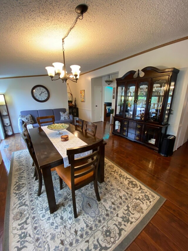 dining area featuring a textured ceiling, ornamental molding, dark hardwood / wood-style floors, and an inviting chandelier