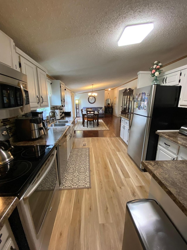 kitchen featuring appliances with stainless steel finishes, white cabinetry, a textured ceiling, light hardwood / wood-style floors, and decorative light fixtures