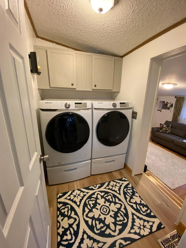 laundry area featuring washing machine and dryer, light wood-type flooring, a textured ceiling, crown molding, and cabinets