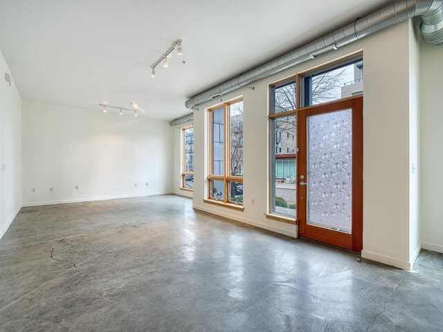 spare room with rail lighting, concrete flooring, and a wealth of natural light