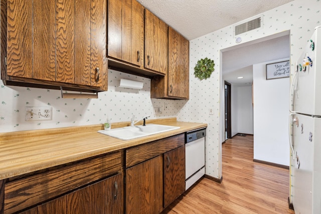 kitchen featuring white appliances, light hardwood / wood-style floors, a textured ceiling, and sink