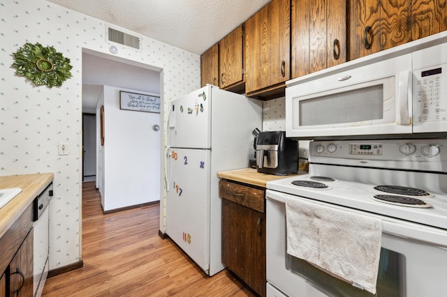 kitchen with light hardwood / wood-style flooring, a textured ceiling, and white appliances