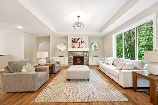 living room with light hardwood / wood-style flooring, a stone fireplace, and a tray ceiling