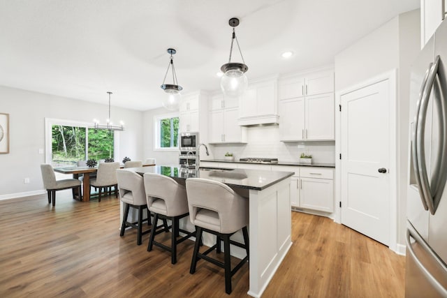 kitchen featuring a breakfast bar area, an island with sink, hanging light fixtures, wood-type flooring, and white cabinets