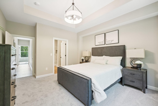 carpeted bedroom with ensuite bath, a chandelier, and a raised ceiling