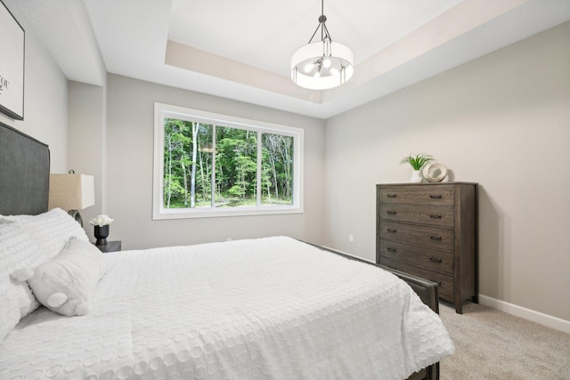 bedroom featuring a notable chandelier, light colored carpet, and a tray ceiling