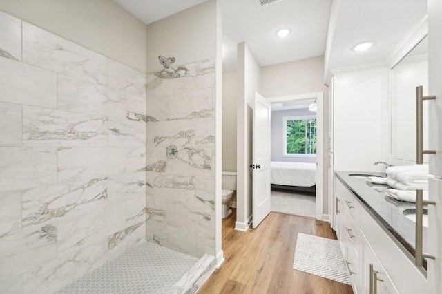 bathroom featuring toilet, hardwood / wood-style floors, vanity, and tiled shower