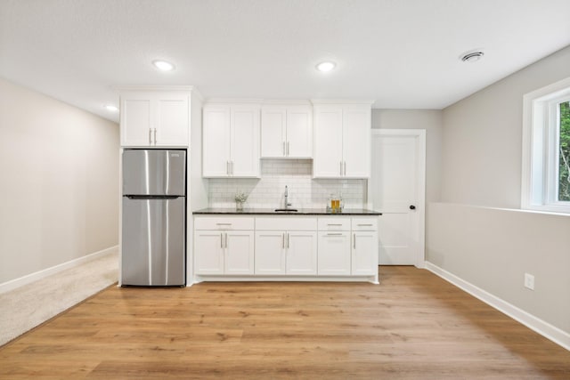 kitchen featuring backsplash, sink, white cabinets, light hardwood / wood-style floors, and stainless steel refrigerator