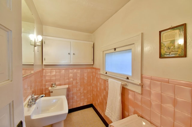 half bath featuring a sink, tile walls, tile patterned flooring, and wainscoting