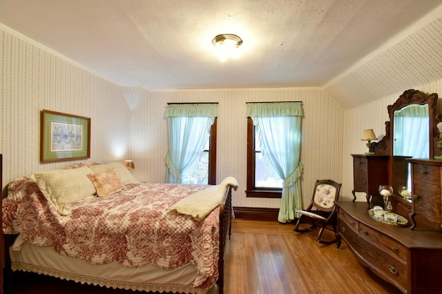bedroom featuring lofted ceiling, wood finished floors, and wallpapered walls