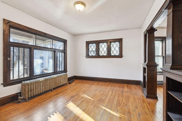 interior space with decorative columns, radiator heating unit, wood-type flooring, and a textured ceiling