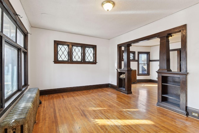 unfurnished living room featuring hardwood / wood-style floors, ornate columns, a textured ceiling, and radiator