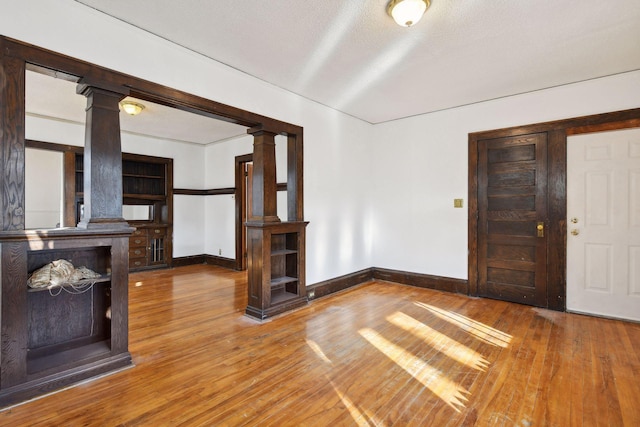 unfurnished living room with a textured ceiling, decorative columns, and hardwood / wood-style flooring