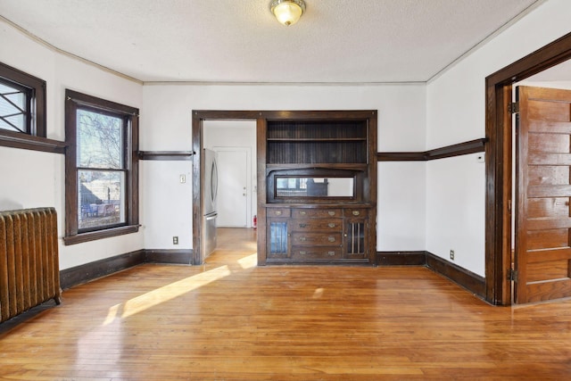 unfurnished living room with radiator, light hardwood / wood-style floors, and a textured ceiling