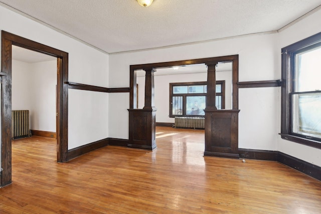 empty room featuring plenty of natural light, ornate columns, a textured ceiling, and radiator