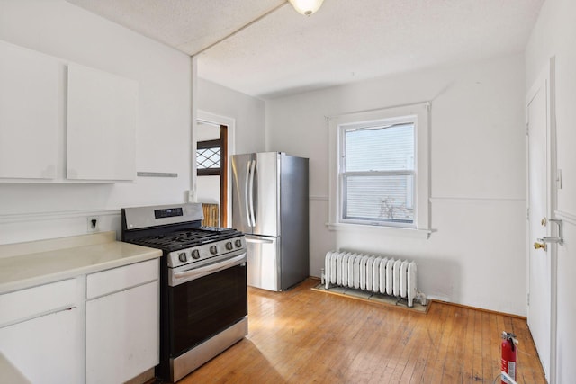 kitchen with light wood-type flooring, a textured ceiling, stainless steel appliances, white cabinets, and radiator heating unit