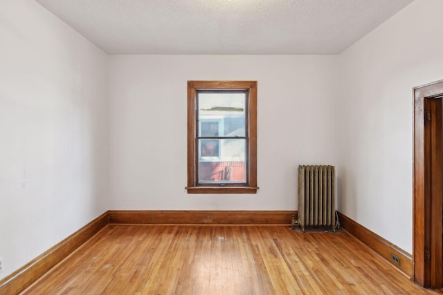 spare room featuring radiator heating unit, a textured ceiling, and light hardwood / wood-style flooring