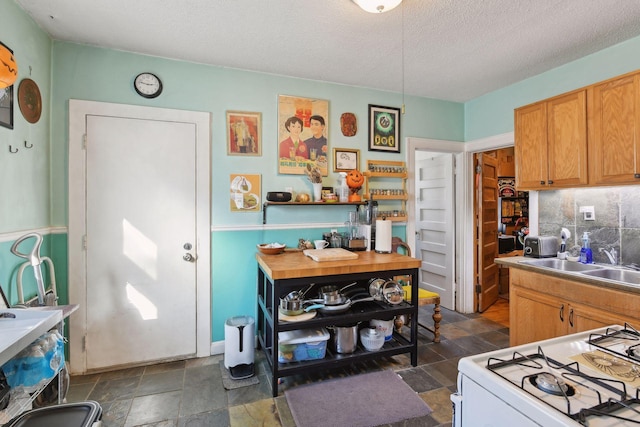 kitchen featuring backsplash, gas range gas stove, sink, and a textured ceiling