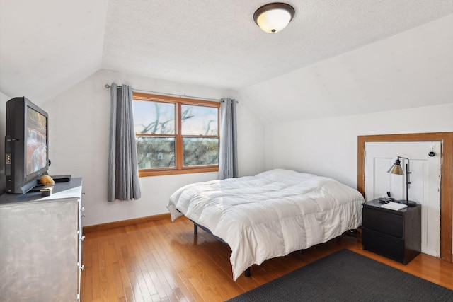 bedroom with hardwood / wood-style flooring, a textured ceiling, and vaulted ceiling