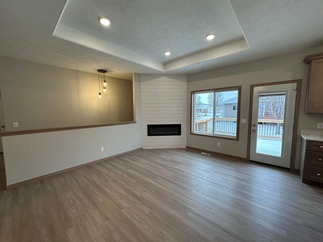 unfurnished living room with a textured ceiling, a raised ceiling, light wood-type flooring, and a fireplace