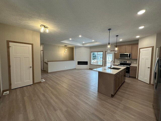 kitchen featuring a center island with sink, a textured ceiling, decorative light fixtures, wood-type flooring, and stainless steel appliances