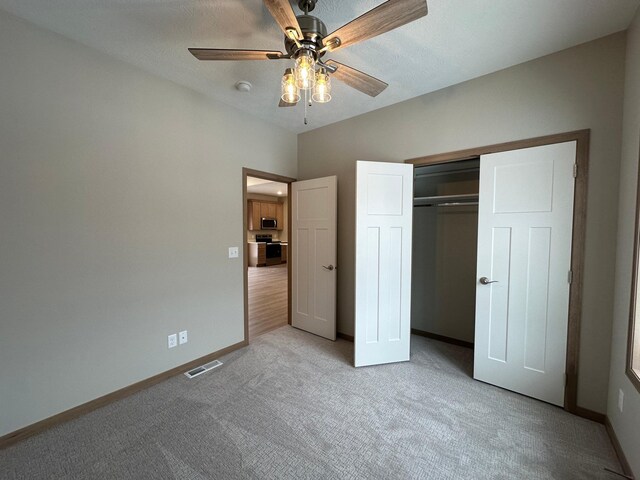 unfurnished bedroom with a textured ceiling, a closet, ceiling fan, and light colored carpet