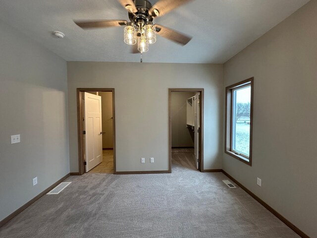 unfurnished bedroom featuring light colored carpet, a spacious closet, a closet, and ceiling fan