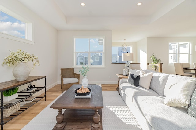 living room featuring a raised ceiling, an inviting chandelier, plenty of natural light, and hardwood / wood-style floors