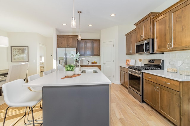 kitchen featuring a kitchen island with sink, sink, a breakfast bar, light wood-type flooring, and appliances with stainless steel finishes