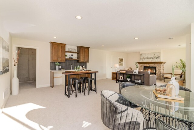 carpeted dining space featuring indoor wet bar and a stone fireplace