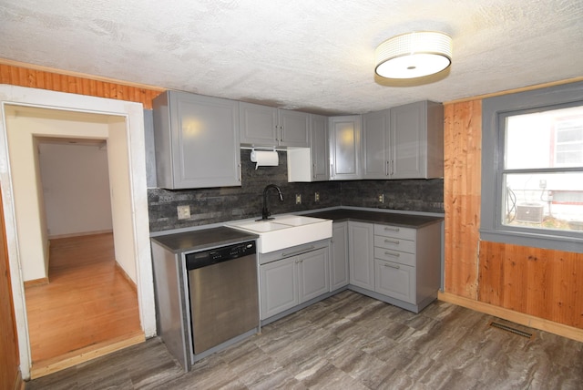 kitchen with gray cabinets, wood walls, stainless steel dishwasher, and dark hardwood / wood-style floors