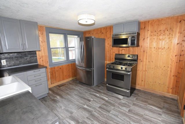 kitchen with a textured ceiling, wooden walls, sink, gray cabinets, and appliances with stainless steel finishes