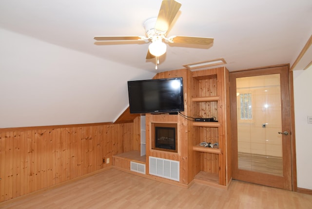 unfurnished living room featuring wood-type flooring, wooden walls, and ceiling fan