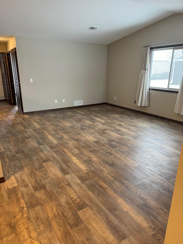 empty room with lofted ceiling, dark wood-type flooring, and a textured ceiling