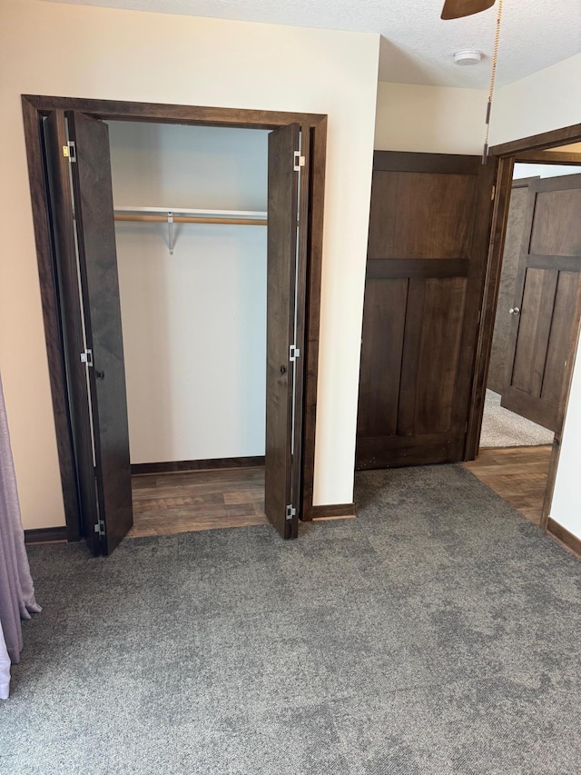 unfurnished bedroom featuring dark carpet, a textured ceiling, a closet, and ceiling fan