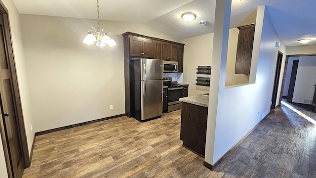 kitchen with lofted ceiling, stainless steel appliances, wood finished floors, dark brown cabinets, and pendant lighting