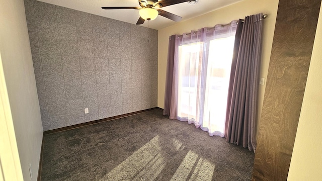 spare room with a ceiling fan, dark colored carpet, and baseboards