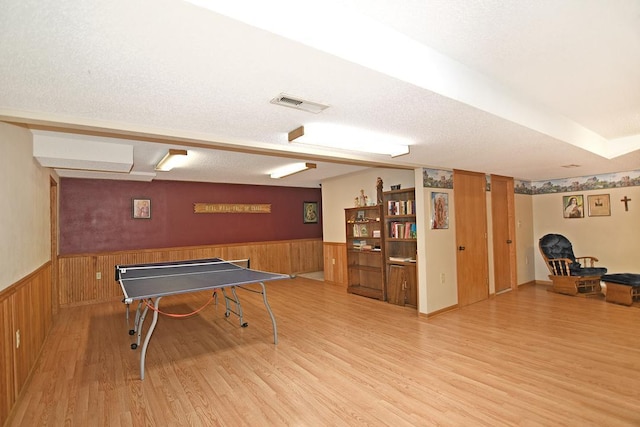 game room with light hardwood / wood-style flooring, wooden walls, and a textured ceiling