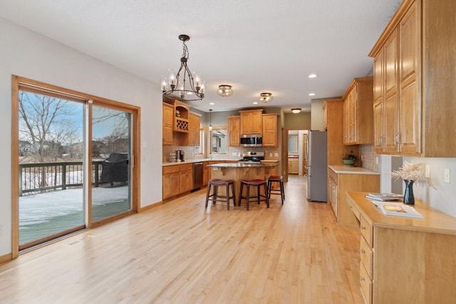 kitchen with pendant lighting, a breakfast bar, appliances with stainless steel finishes, a kitchen island, and light wood-type flooring