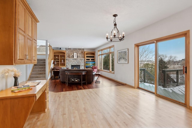 home office featuring a stone fireplace, a notable chandelier, and light hardwood / wood-style flooring