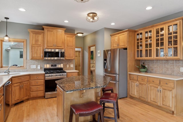 kitchen with appliances with stainless steel finishes, sink, hanging light fixtures, a center island, and light hardwood / wood-style floors