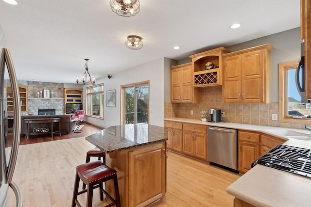 kitchen with a kitchen island, appliances with stainless steel finishes, pendant lighting, decorative backsplash, and light hardwood / wood-style floors