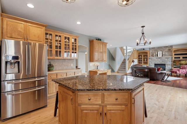 kitchen with a center island, a kitchen bar, stainless steel fridge with ice dispenser, dark stone counters, and light wood-type flooring