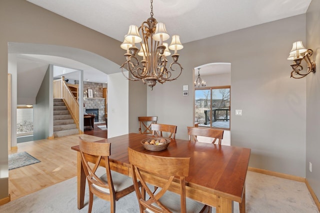 dining space with an inviting chandelier, a stone fireplace, and light hardwood / wood-style floors