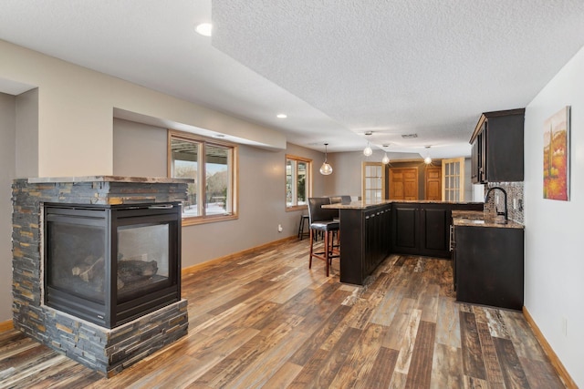 kitchen featuring a breakfast bar area, dark hardwood / wood-style floors, a textured ceiling, a kitchen island, and a stone fireplace