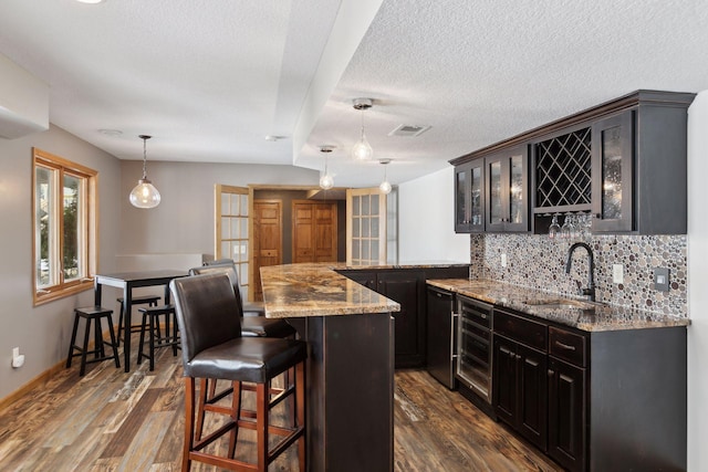 kitchen featuring sink, hanging light fixtures, a kitchen breakfast bar, a center island, and wine cooler