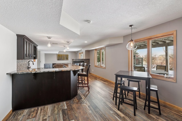 kitchen featuring a kitchen bar, dark brown cabinetry, kitchen peninsula, light stone countertops, and dark wood-type flooring