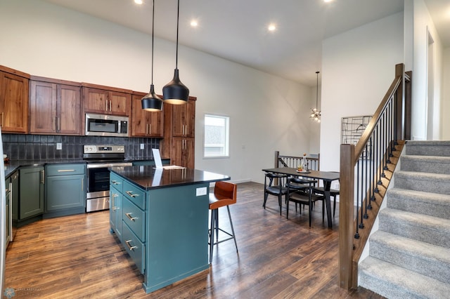 kitchen with appliances with stainless steel finishes, a kitchen island, decorative light fixtures, high vaulted ceiling, and dark hardwood / wood-style floors