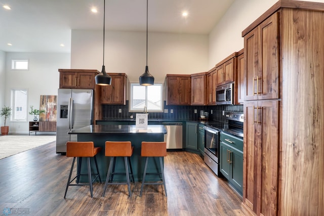 kitchen featuring appliances with stainless steel finishes, a kitchen island, backsplash, hanging light fixtures, and dark wood-type flooring